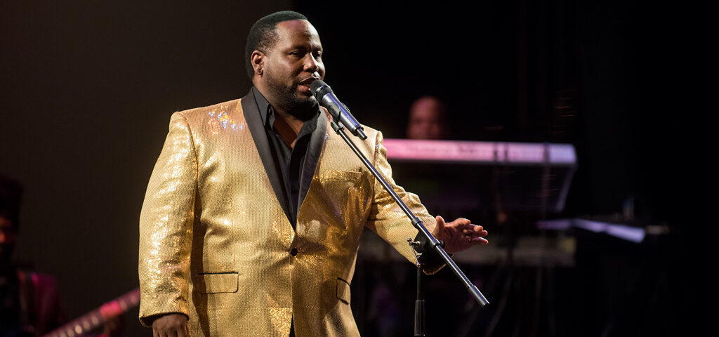 A man in gold jacket holding a microphone.