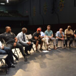 A group of men sitting in chairs on the stage.